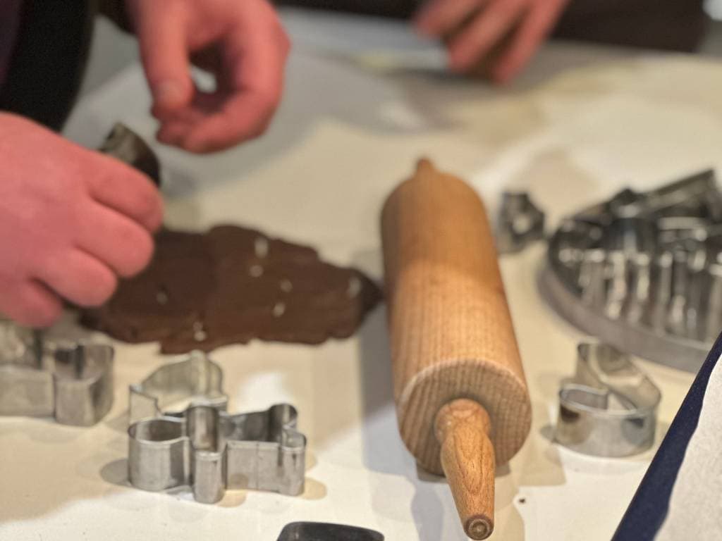 Es wird ein dunkler Teig ausgestochen. Man sieht Plätzchenausstecher und ein Nudelholz.