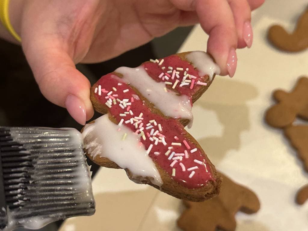 Es wird ein Plätzchen dekoriert mit weißem und rotem Zuckerguss, sowie bunten Streuseln.